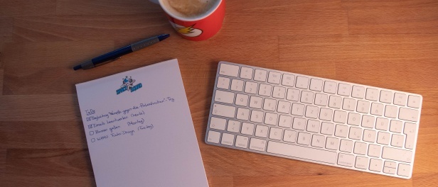 handschriftliche ToDo-Liste neben weißer Tastatur, Stift und roter Kaffeetasse